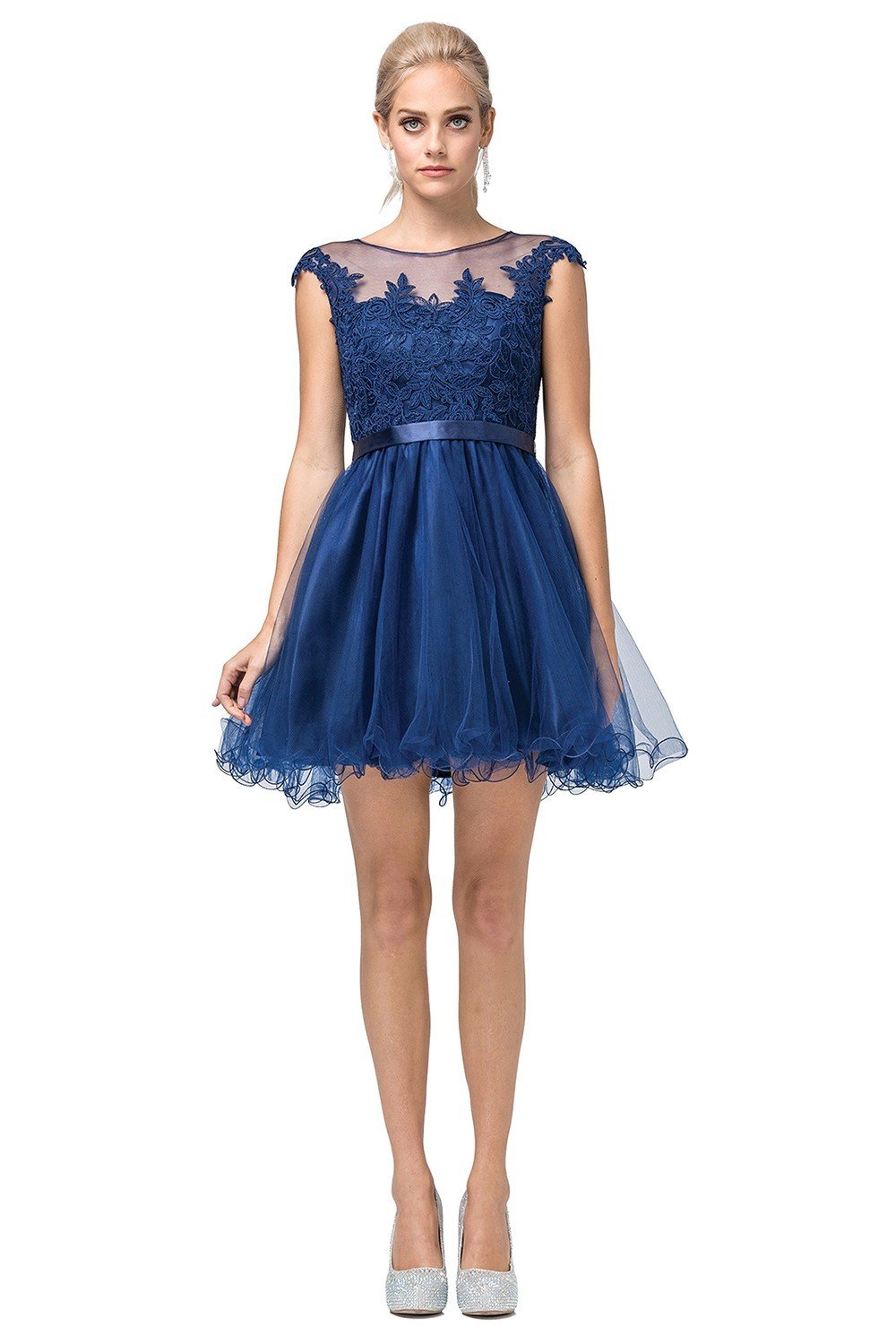 A woman in a Lace-Applique-Bodice Short Homecoming Dress with an embroidered lace bodice, tulle skirt, and cap sleeves pairs it with silver heels while standing against a white background.